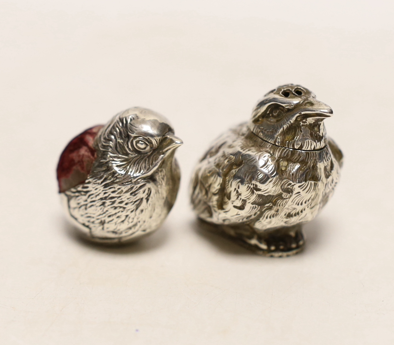 An Edwardian novelty silver pin cushion, modelled as a hatching chick, Sampson Mordan & Co, Chester, 1907, height 33mm and a late Victorian silver chick pepperette, London, 1883.